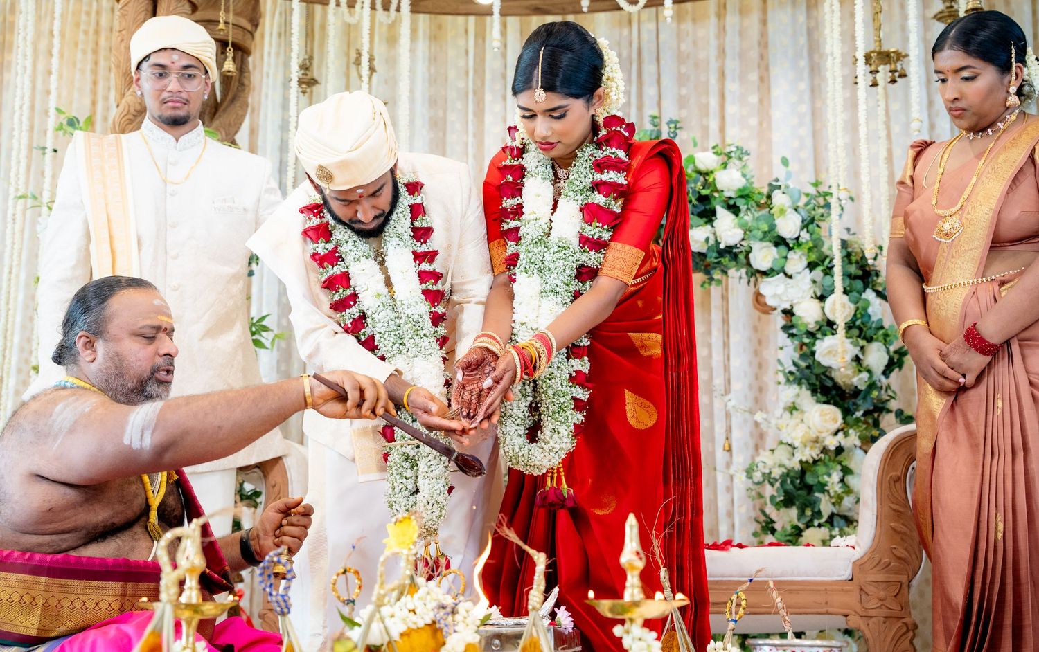 Indian wedding couple in floral garlands perform sacred rituals at beautifully decorated mandap.