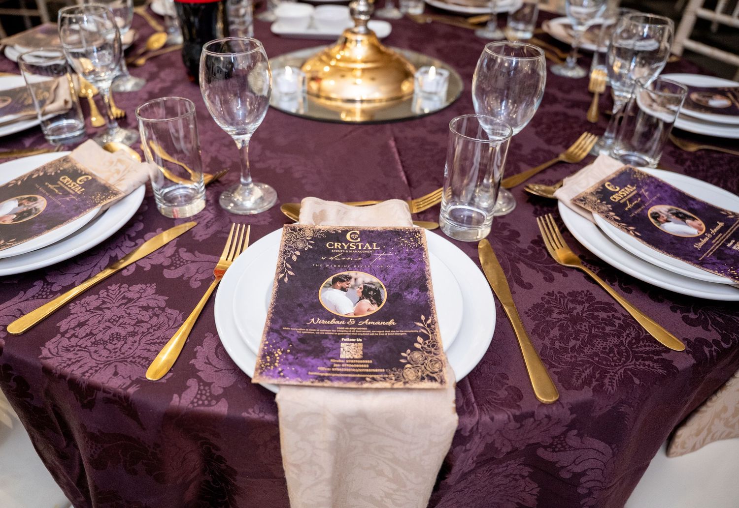 Elegant wedding reception table set with purple damask linen, gold cutlery, and menus.