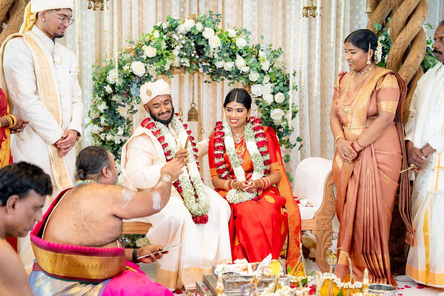Priest conducts sacred Hindu wedding rituals as bride and groom sit together on decorated ceremonial stage.