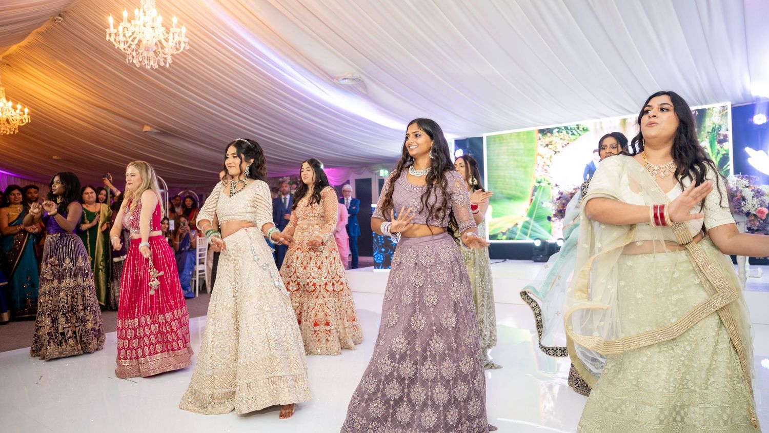 Women in colorful lehengas perform a choreographed dance at an Indian wedding celebration.
