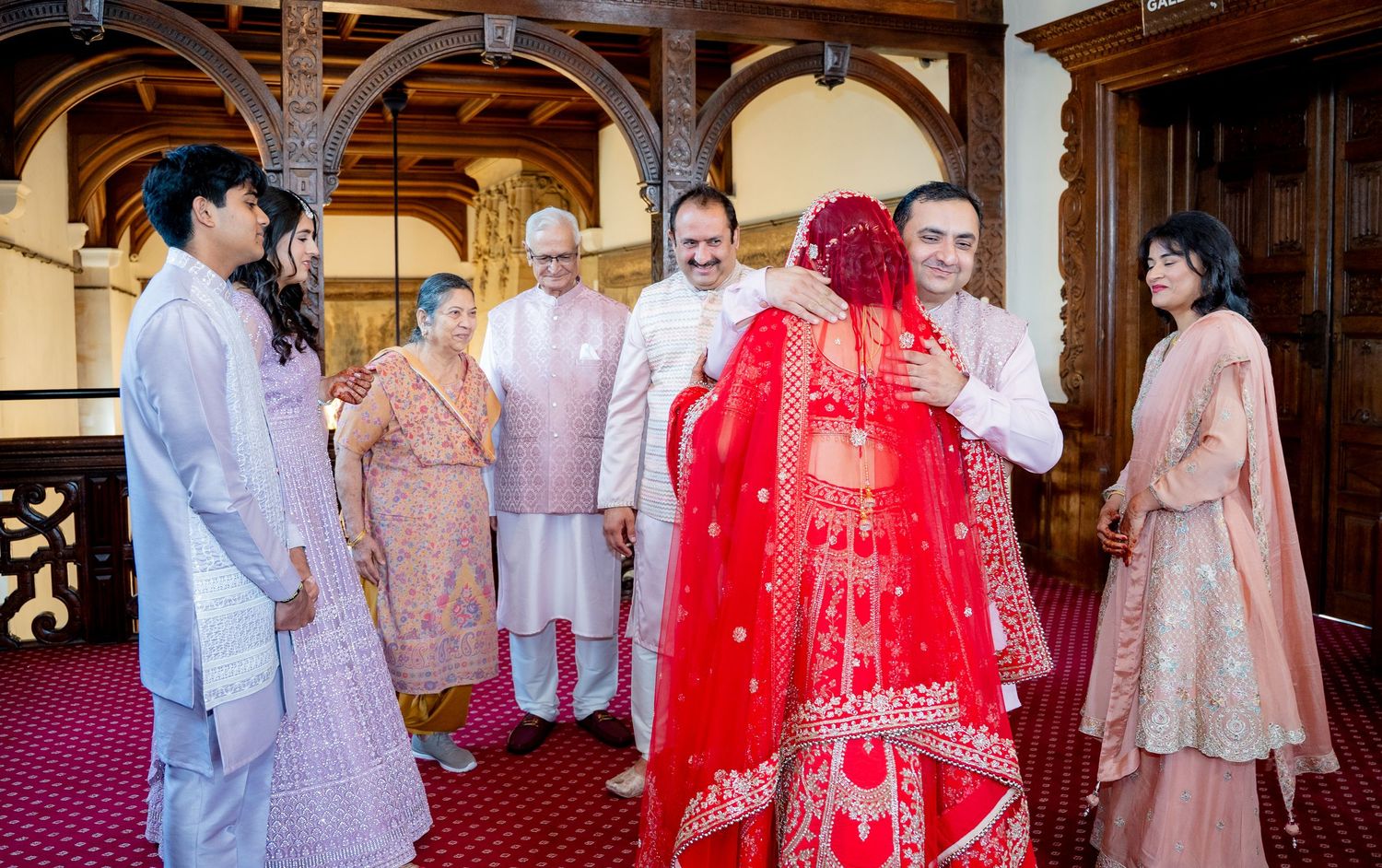Indian bride in red lehenga embracing family member during traditional wedding ceremony indoors.