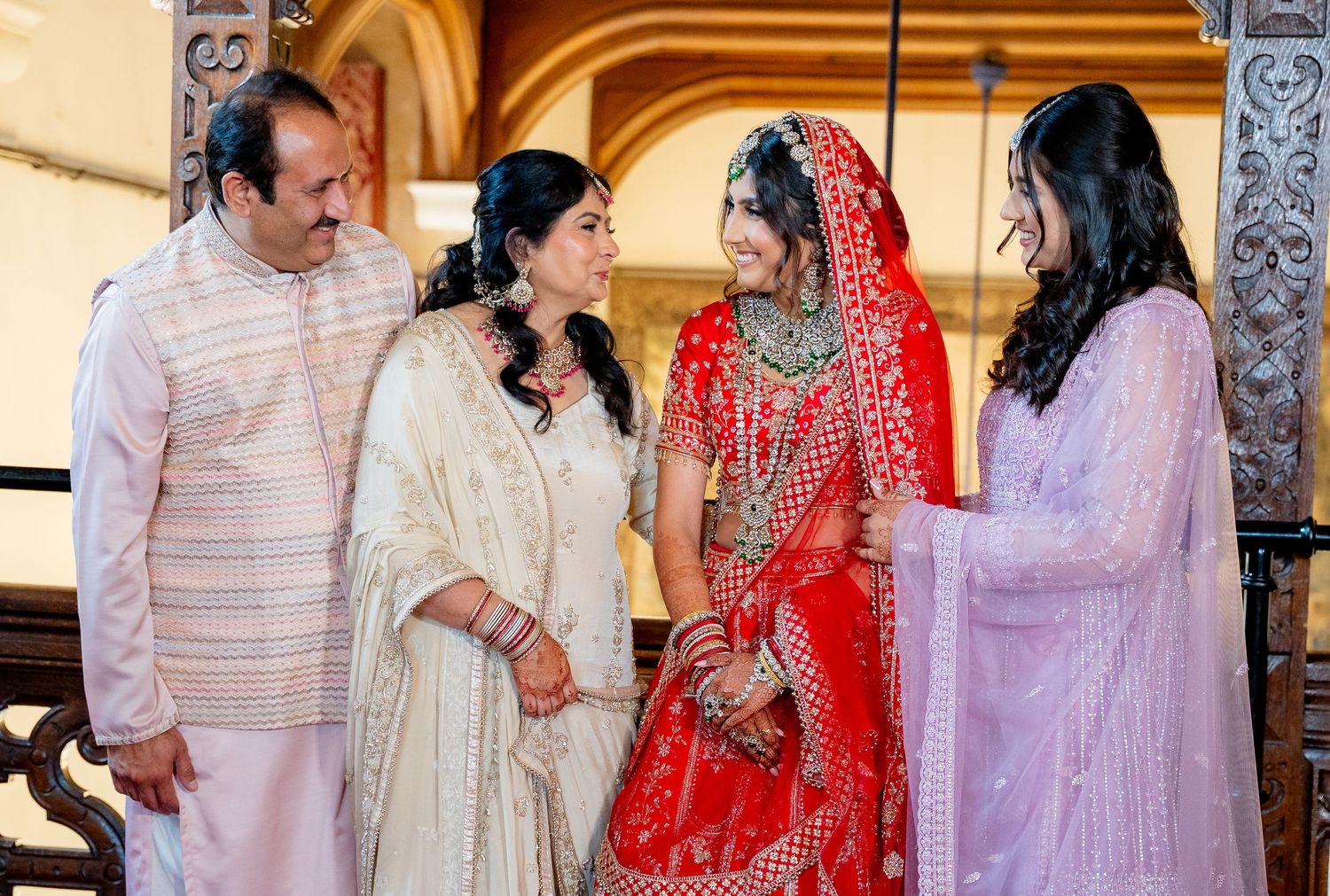 Indian bride in red lehenga shares a warm moment with family members in traditional attire.