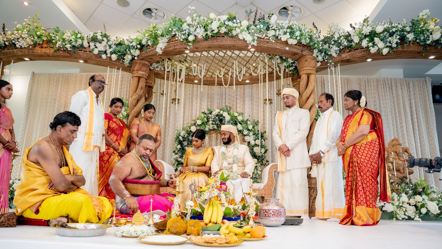 A traditional Hindu wedding ceremony with bride and groom performing rituals surrounded by family members in traditional attire.
