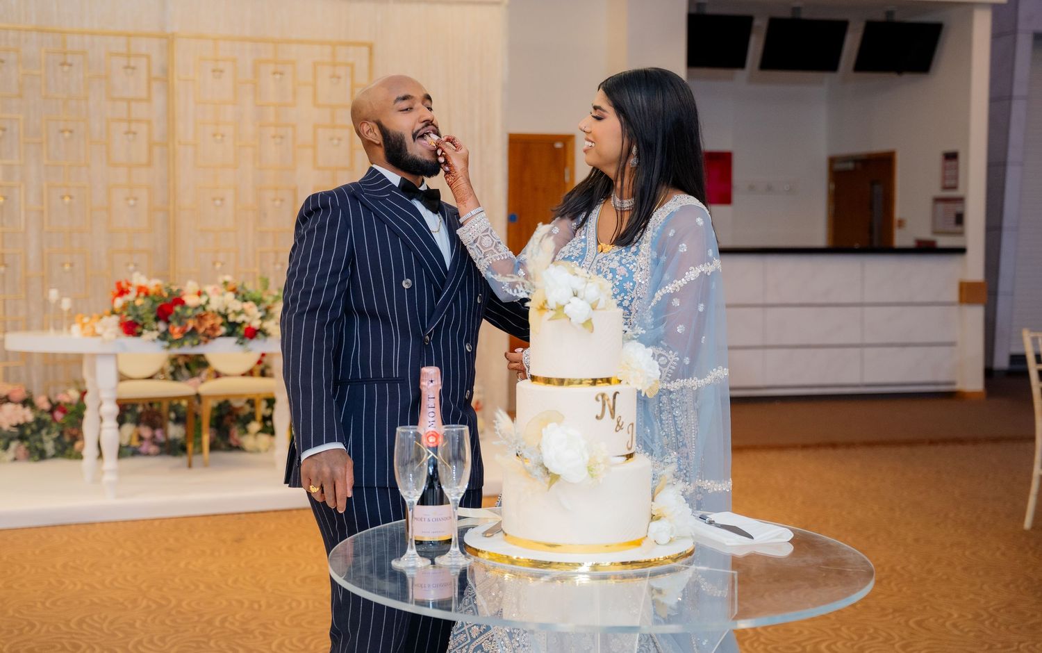 Bride playfully feeds groom wedding cake beside champagne at elegant reception venue.