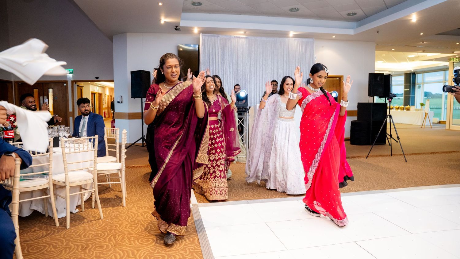 Women in colorful sarees dancing at an Indian wedding reception celebration.