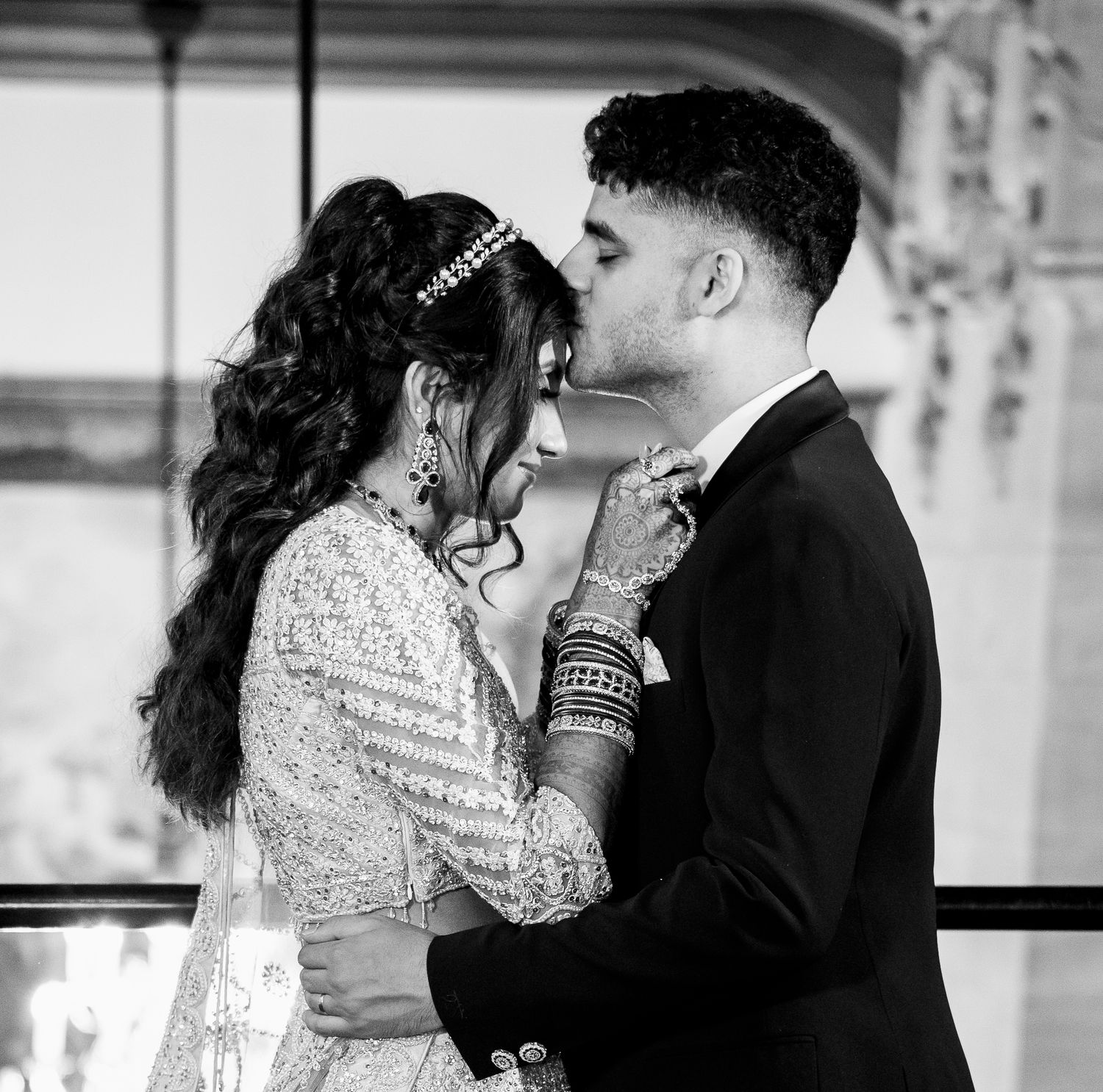Black and white photo of a bride and groom sharing a romantic moment, with the bride in a beaded gown and bangles.