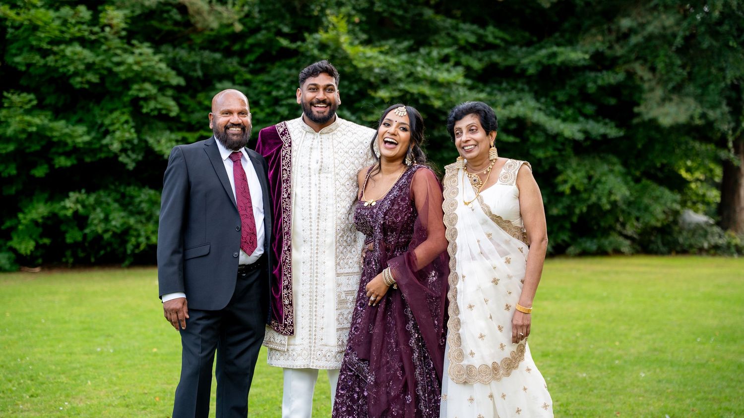 Family of four posing together at an Indian wedding outdoors, wearing traditional and formal attire on a green lawn.