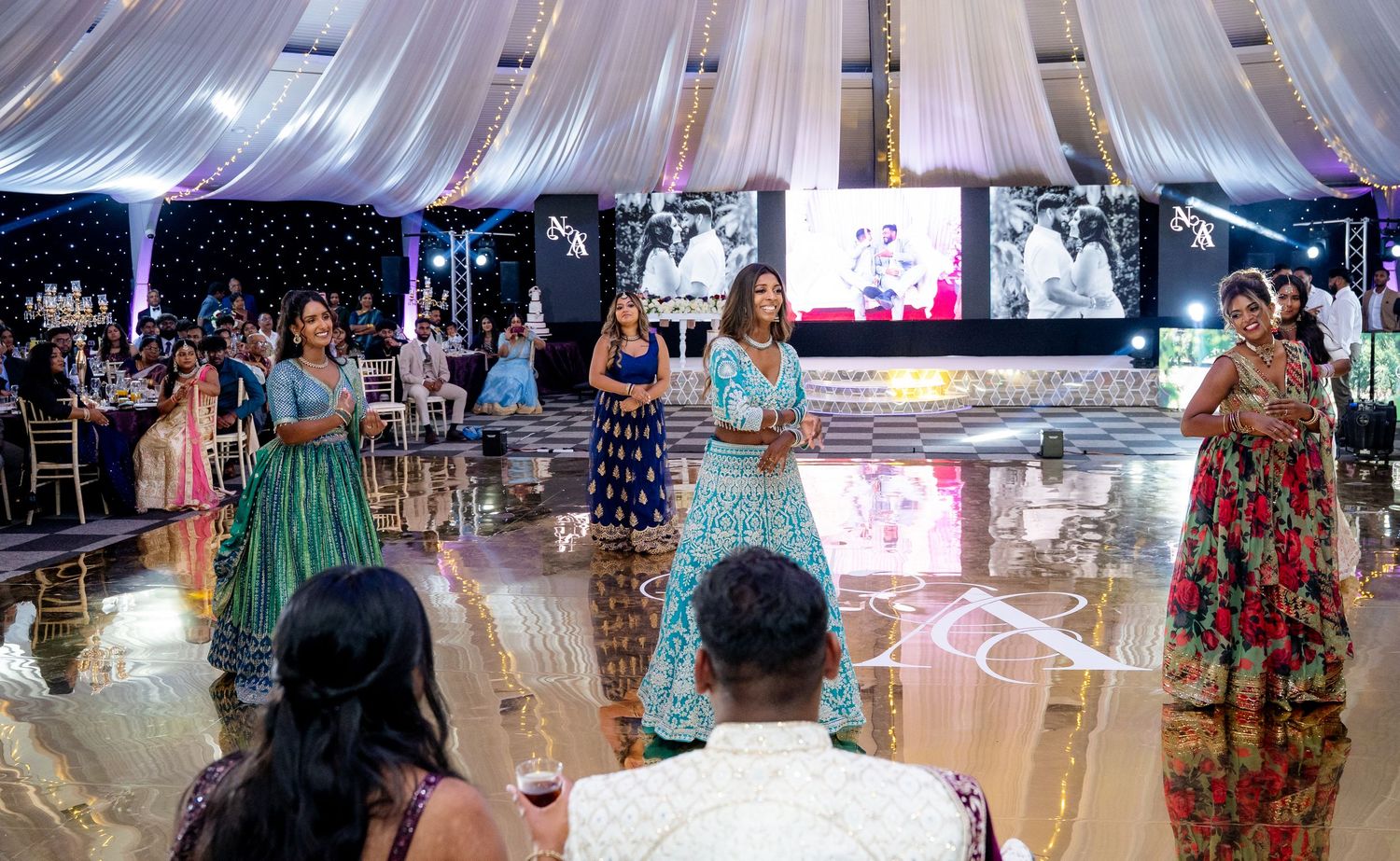 Women in colorful Indian outfits performing a dance at an elegant wedding reception.