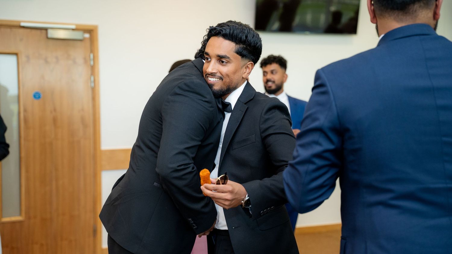 Two young men in suits sharing a warm hug at a formal celebration event.