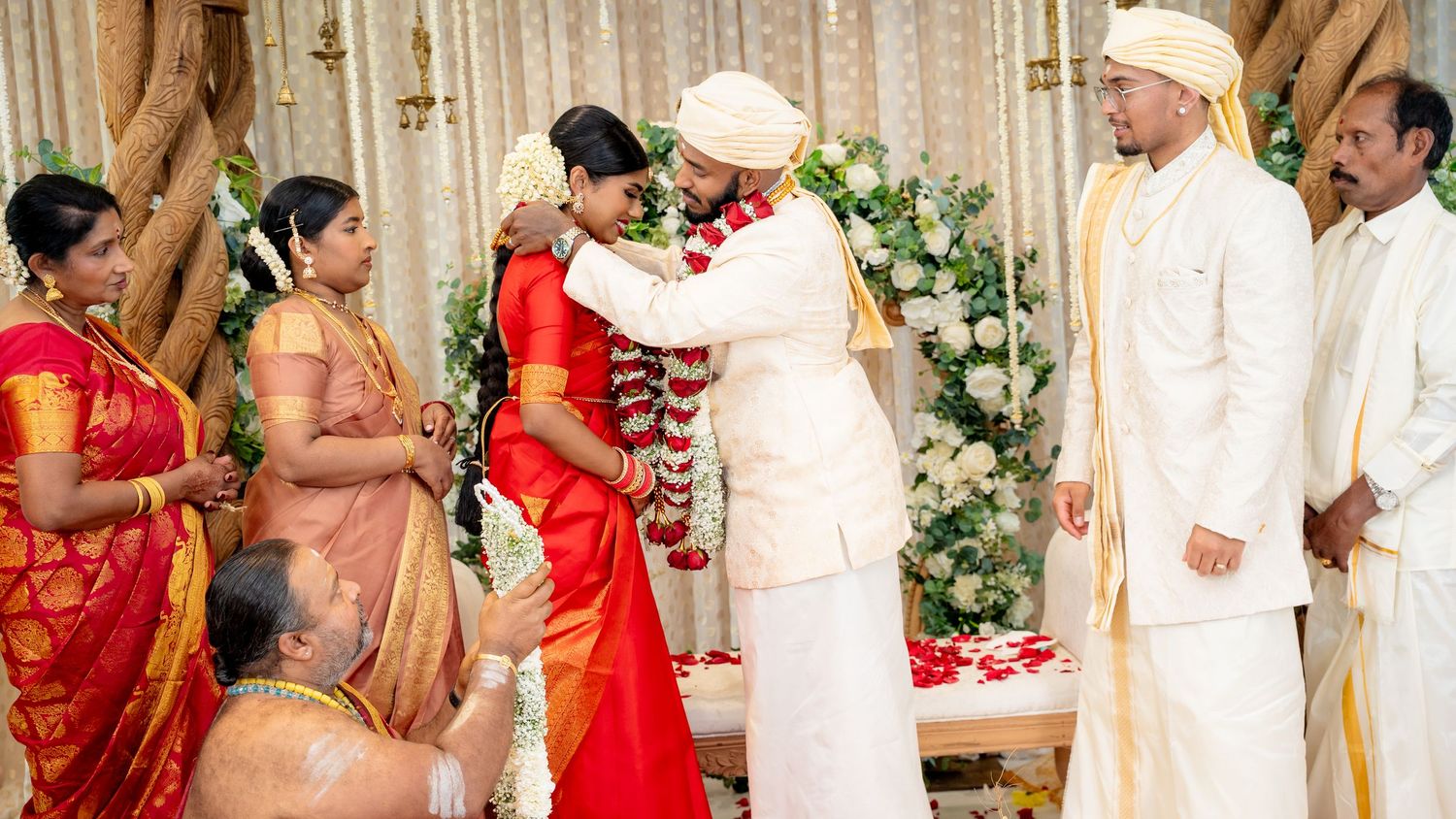 Couple embraces during garland exchange at a vibrant South Indian wedding ceremony with guests watching.