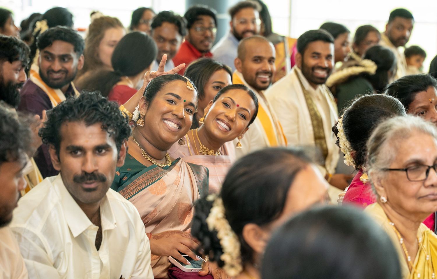 Guests smiling and laughing during a traditional South Indian wedding ceremony in a decorated hall.