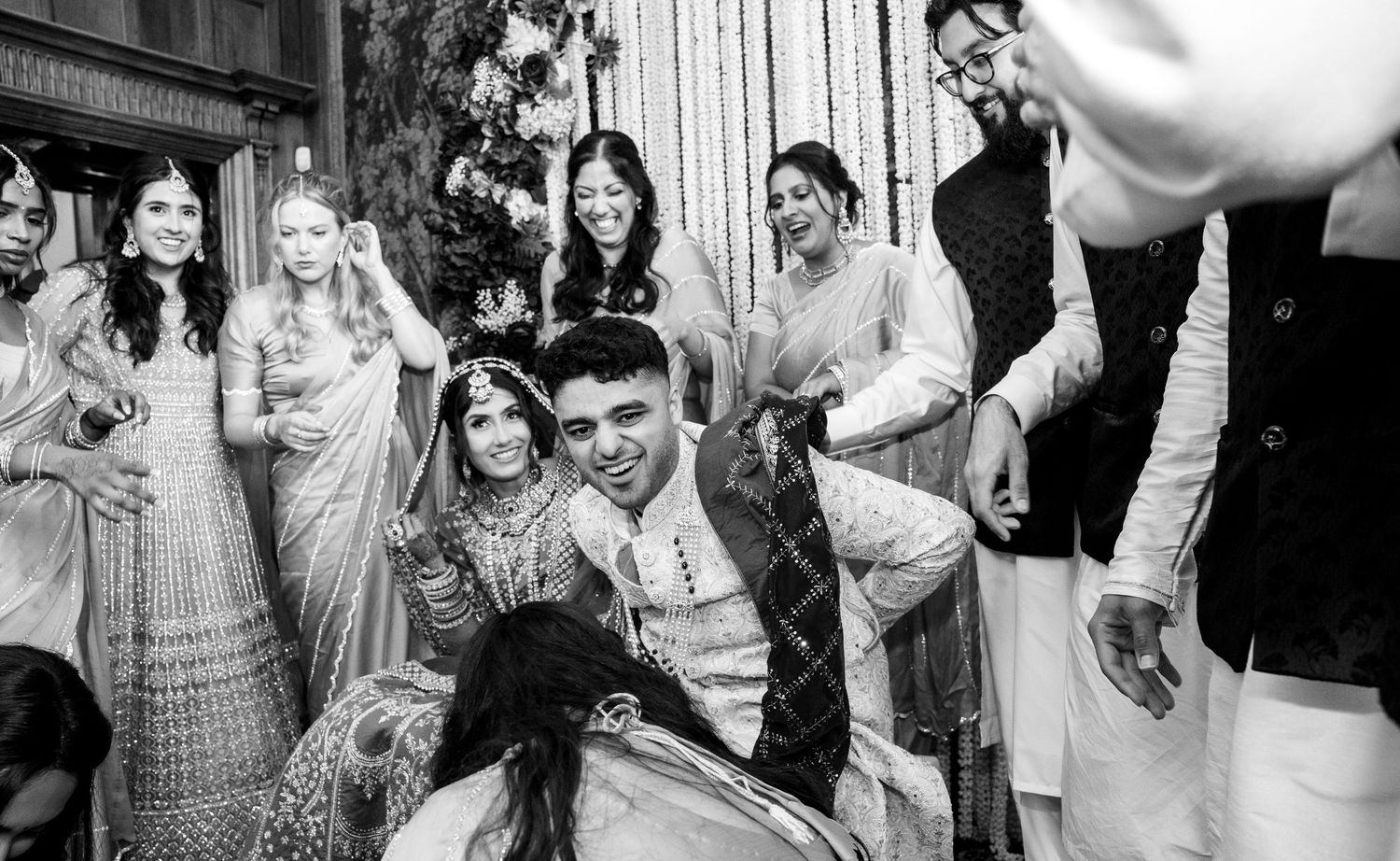 Black and white photo of joyful Indian wedding ceremony moment with bride and groom surrounded by guests.