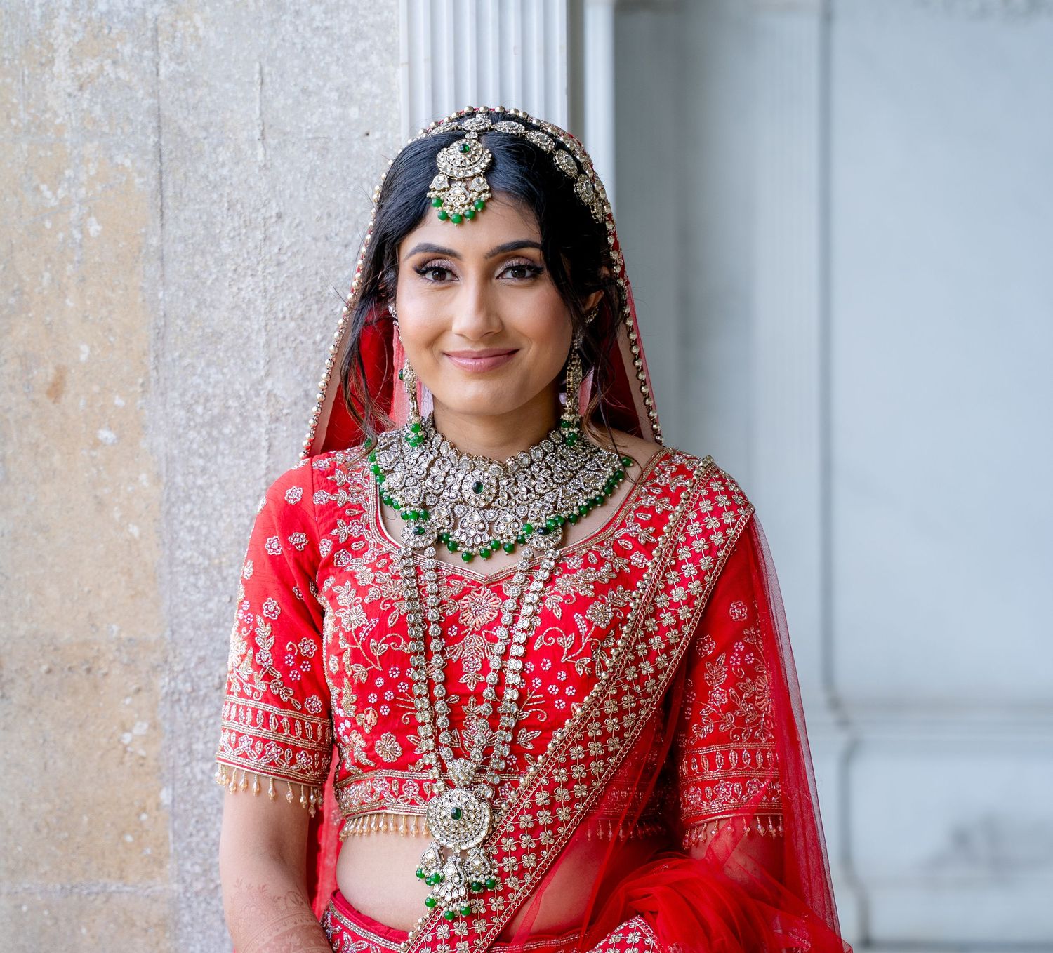 Indian bride in red lehenga with silver jewelry, maang tikka, and dupatta, smiling elegantly.