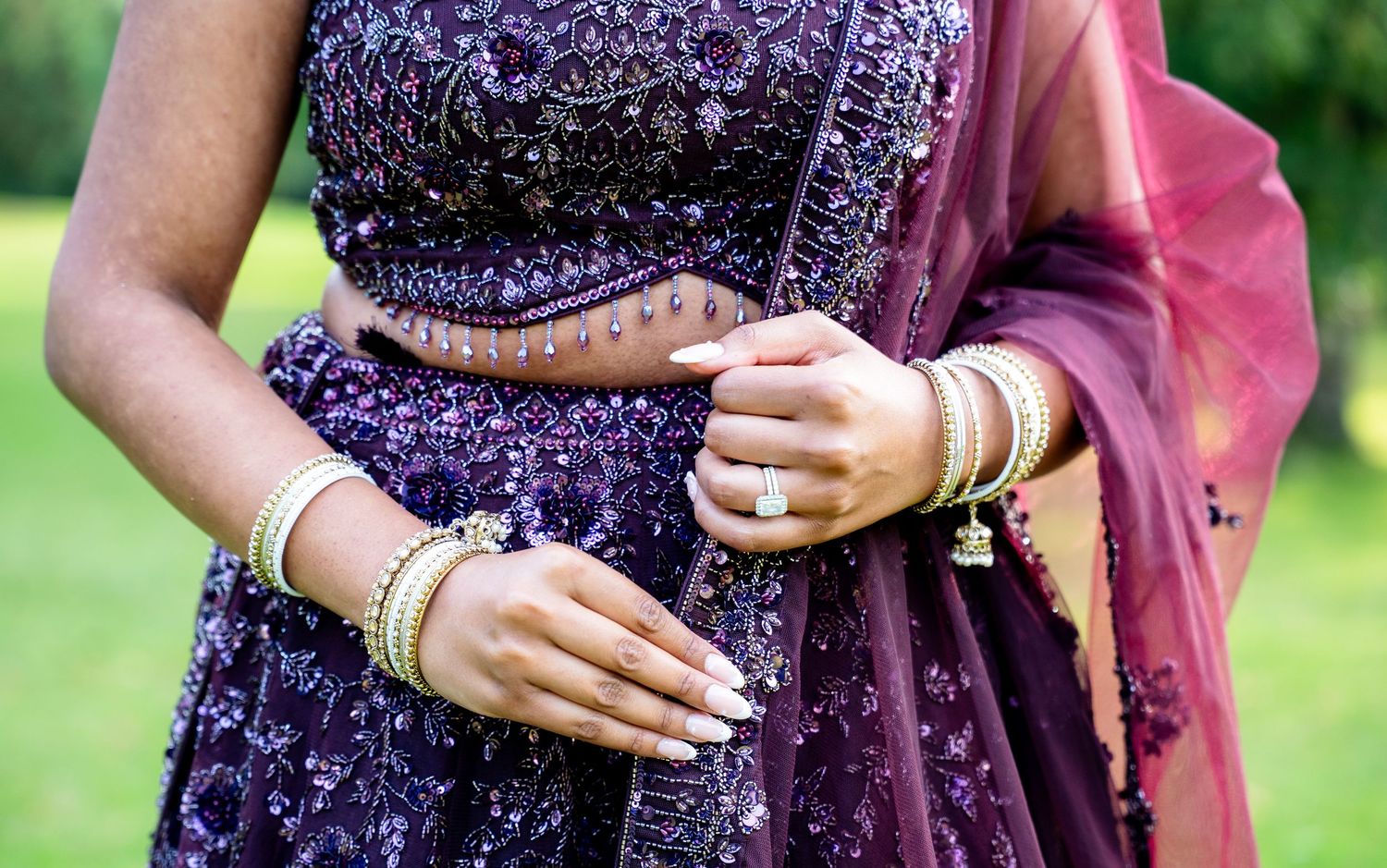 Woman wearing ornate purple embroidered lehenga with gold bangles and rings, traditional Indian bridal attire.
