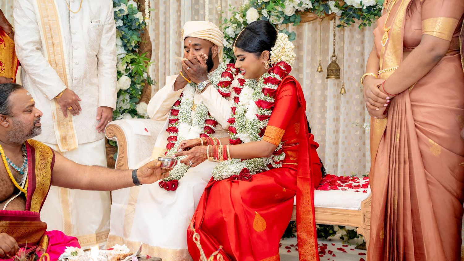 Couple participates in sacred South Indian Hindu wedding rituals with priest and family on decorated stage.