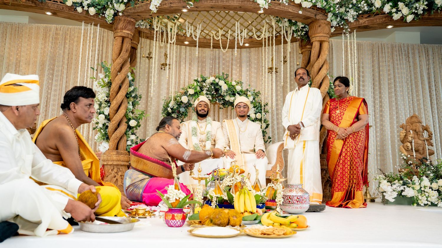 Family and priests gather around the groom during sacred Hindu wedding rituals at a floral mandap.