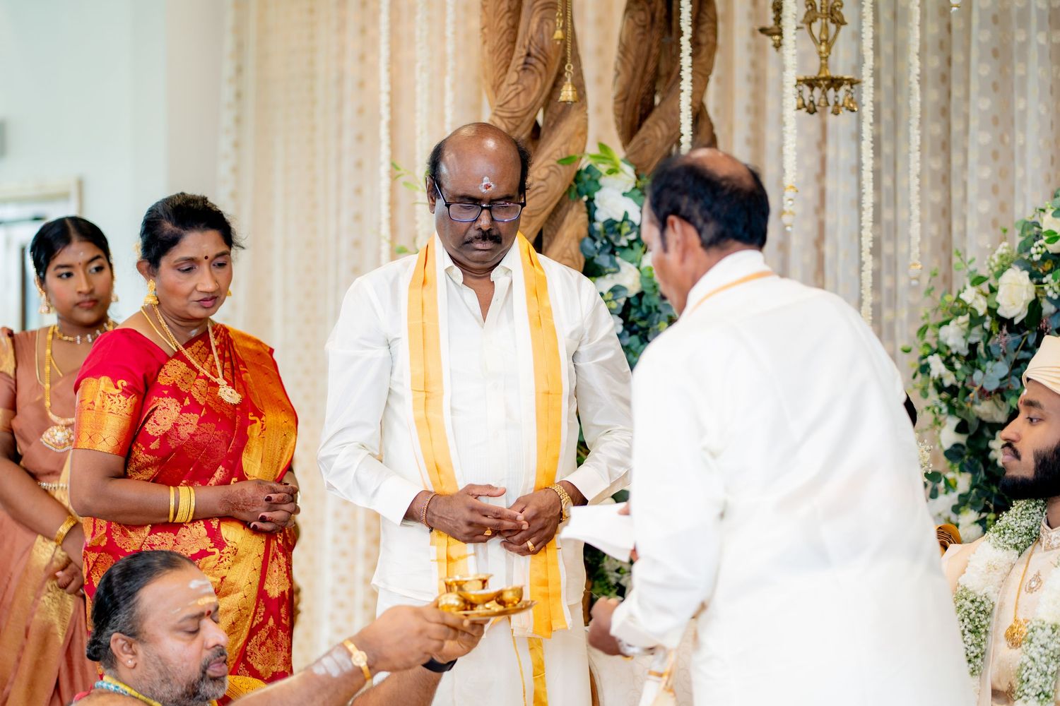 South Indian wedding guest in white dhoti with yellow shawl participating in traditional Hindu ceremony rituals.