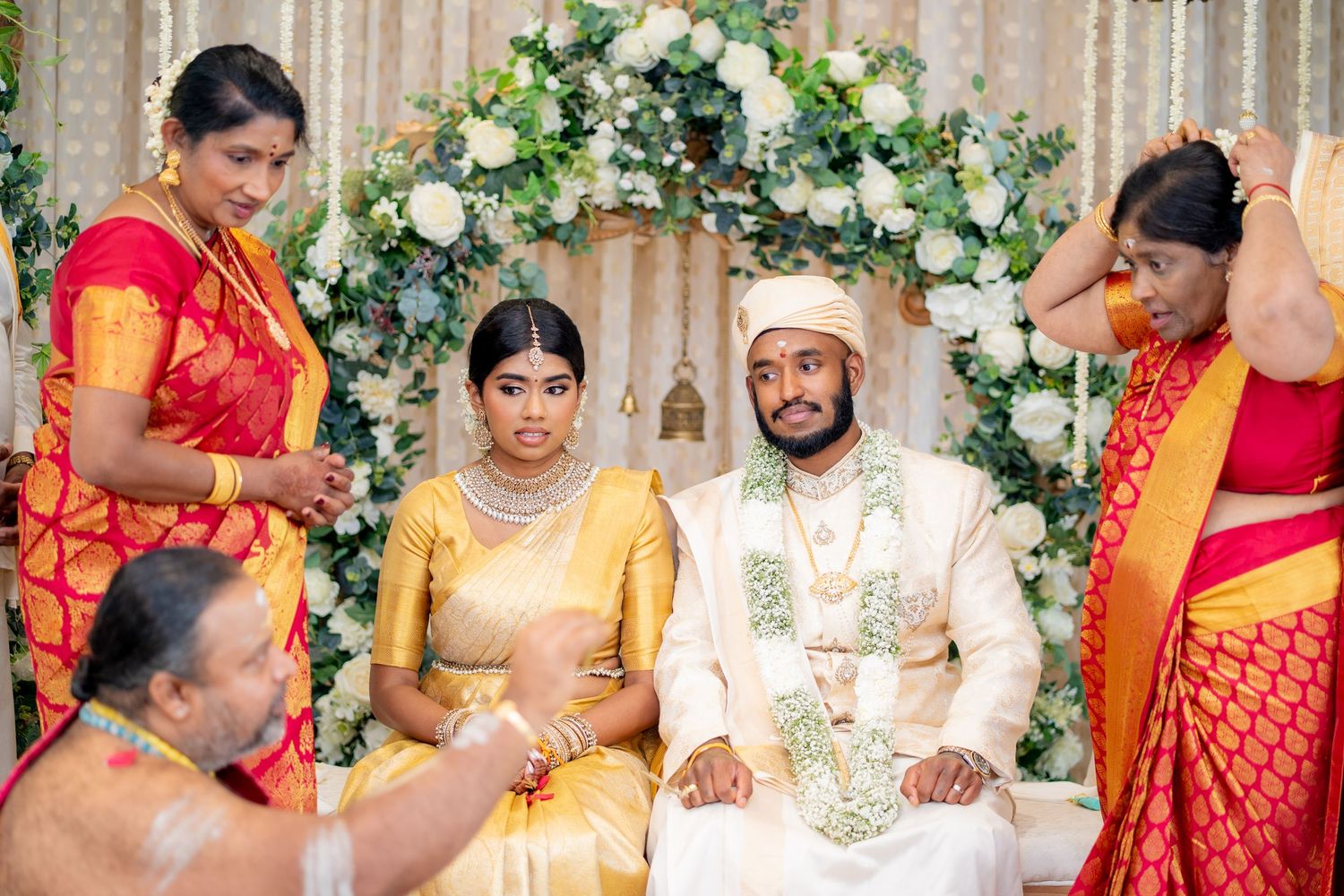 South Indian bride and groom seated at wedding mandap surrounded by family members in colorful traditional attire.