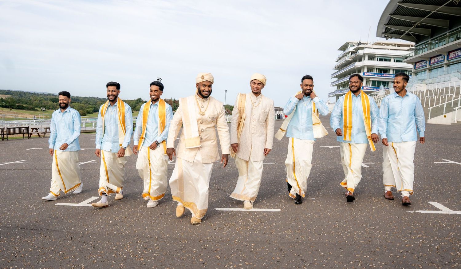 Groom and groomsmen in traditional Indian attire walking confidently at an outdoor venue.