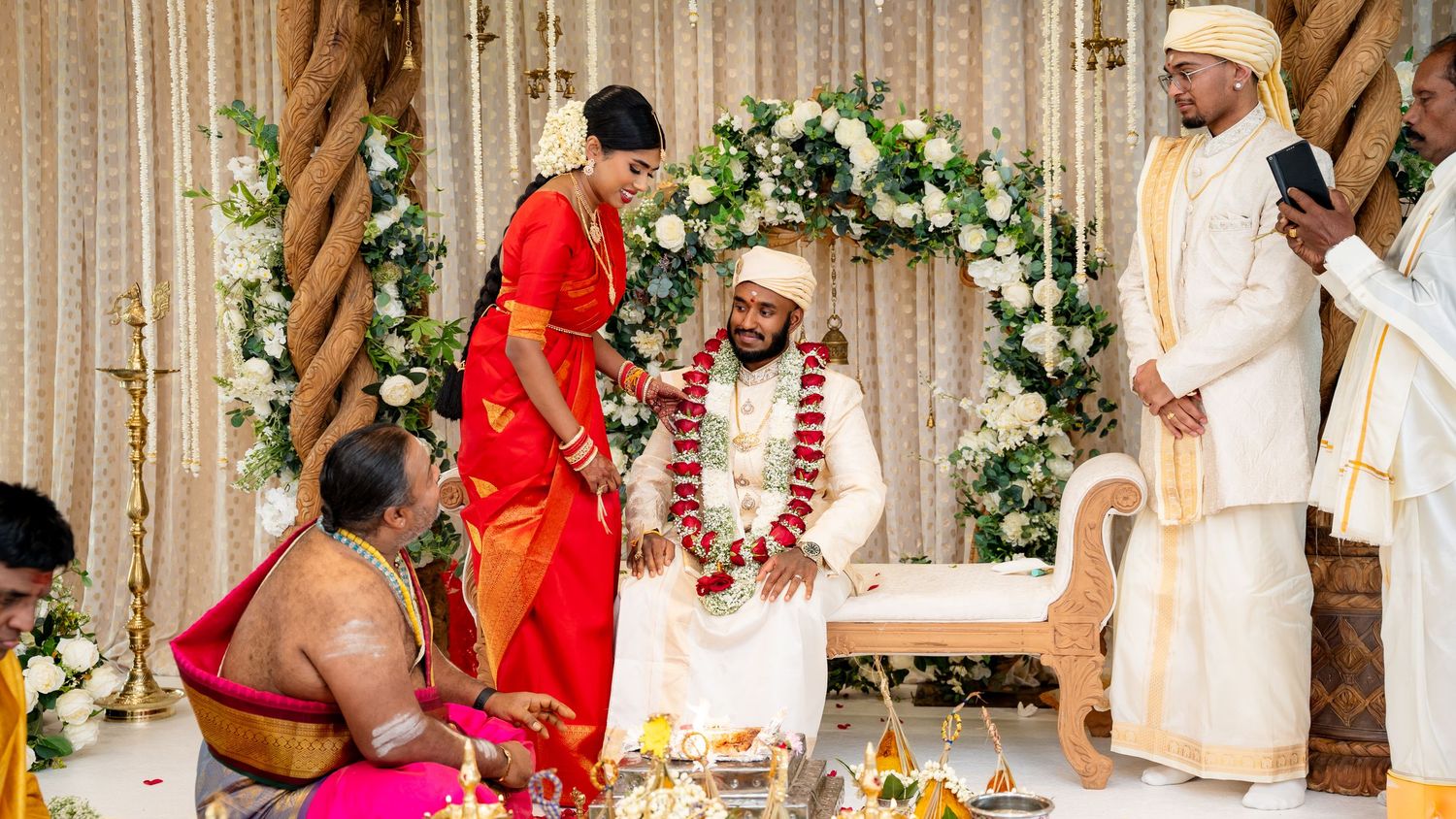 Bride in red saree and groom in white exchange varmala garlands at South Indian wedding.