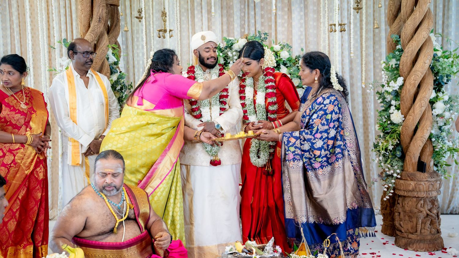 South Indian Hindu wedding ceremony with family blessing couple during garland exchange on decorated mandap stage.