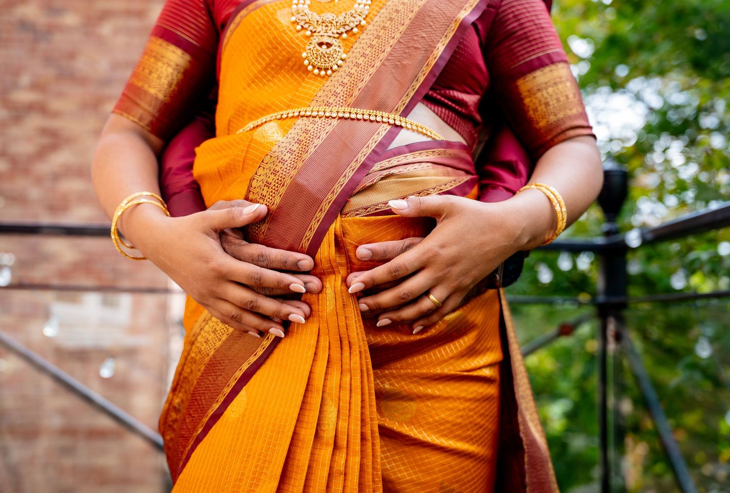 Woman wearing a vibrant orange and red silk saree with gold jewelry and bangles, traditional Indian attire.