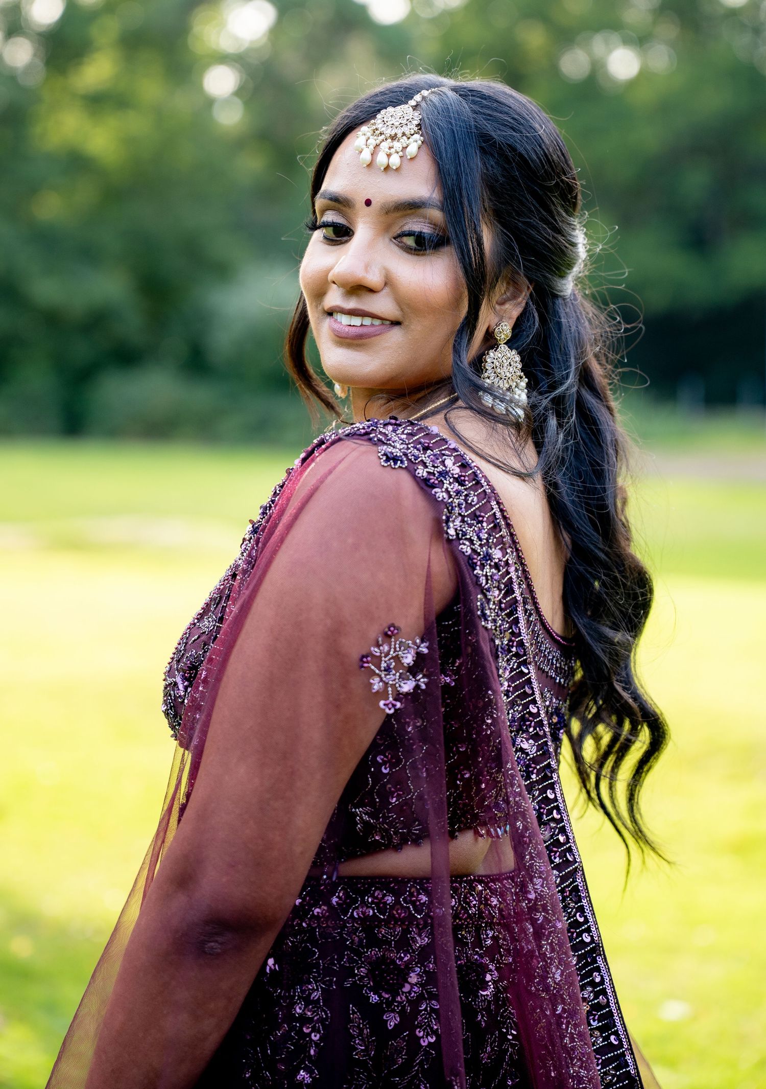 Beautiful woman in backless purple embroidered lehenga with traditional jewelry smiling outdoors.