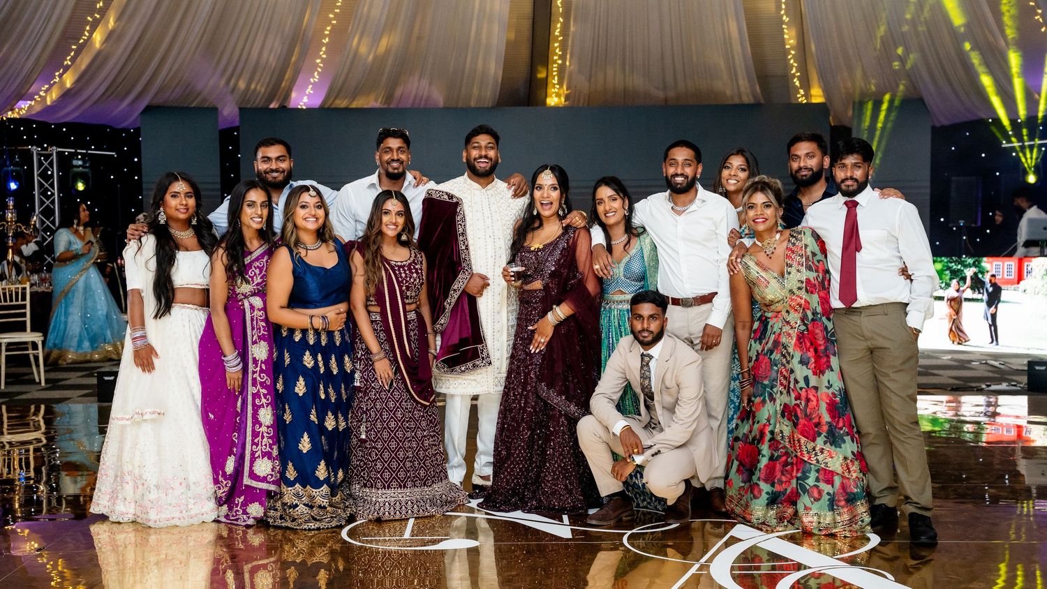Large group of elegantly dressed guests posing together at an Indian wedding reception celebration.