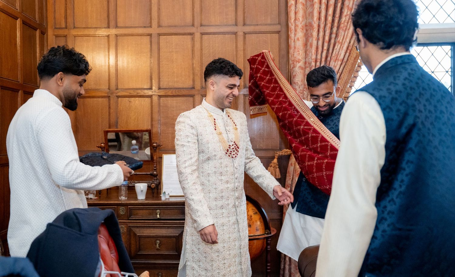 Groom in white sherwani laughs with groomsmen during Indian wedding getting-ready preparations.