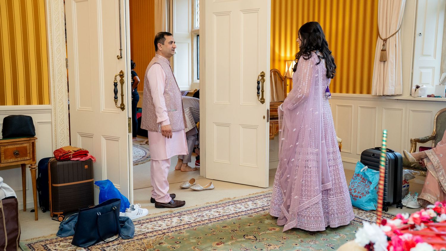 Indian couple in traditional pink and lavender outfits sharing moment in elegant wedding prep room.