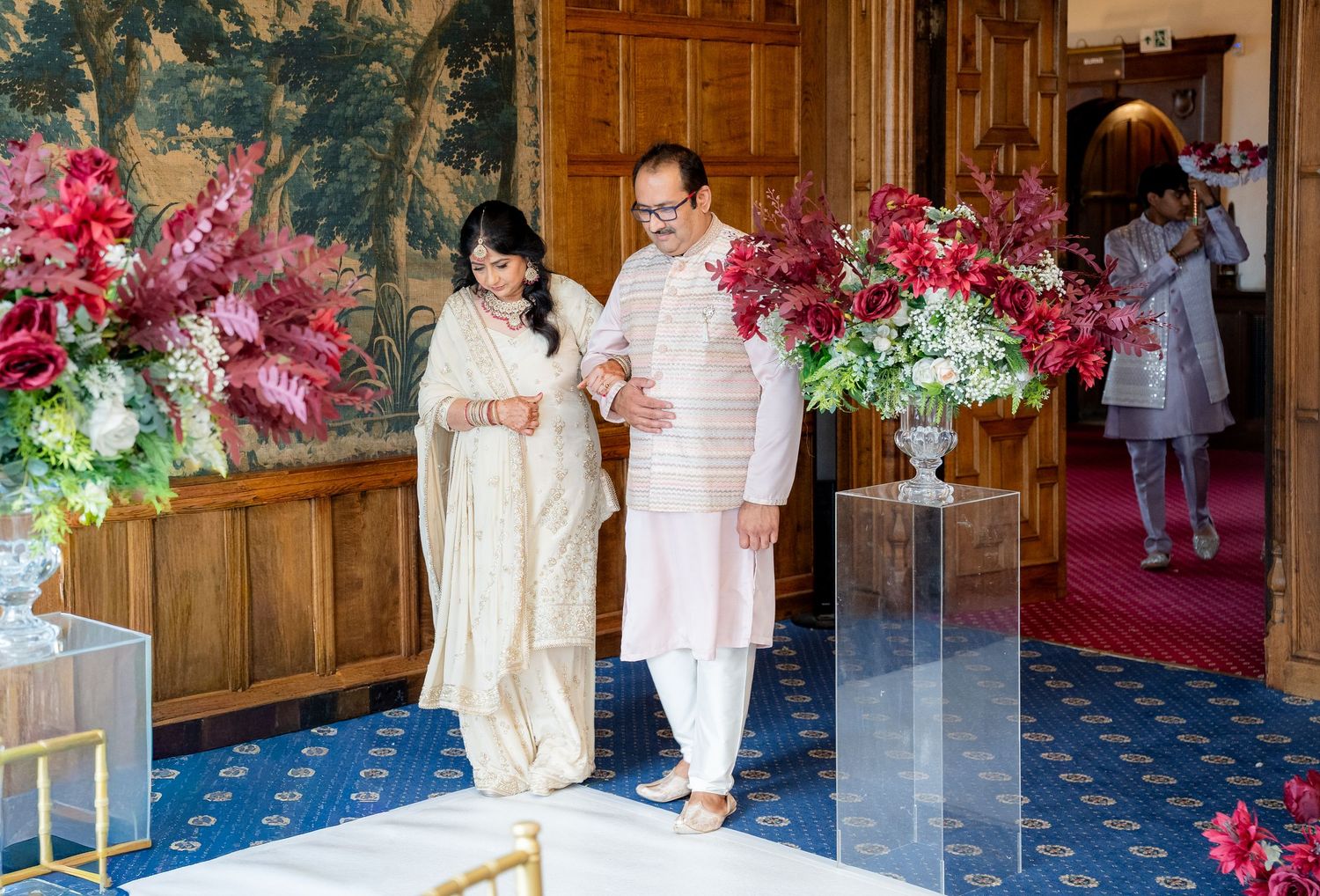 Couple in traditional Indian attire walking through floral decorated wedding venue entrance.