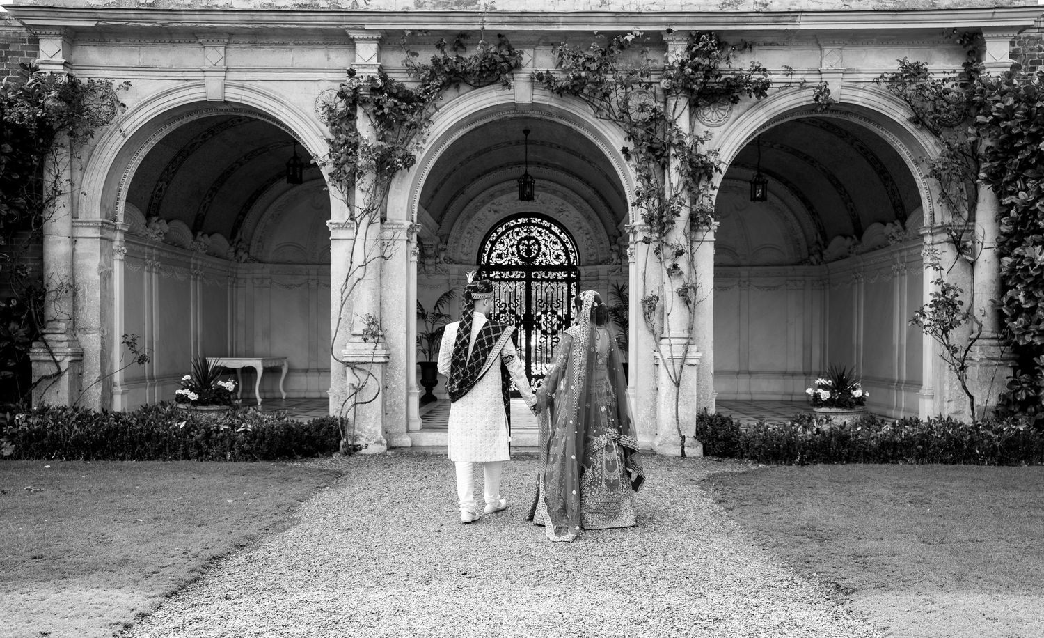 Bride and groom standing together in front of elegant stone archways at a historic venue in black and white photography.