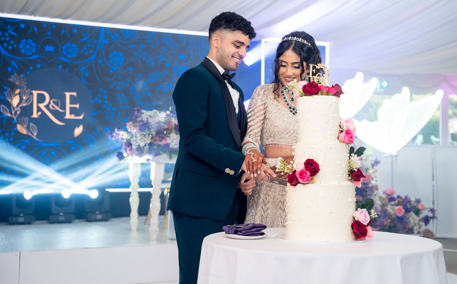 Bride and groom cutting their elegant four-tier white wedding cake decorated with red roses.
