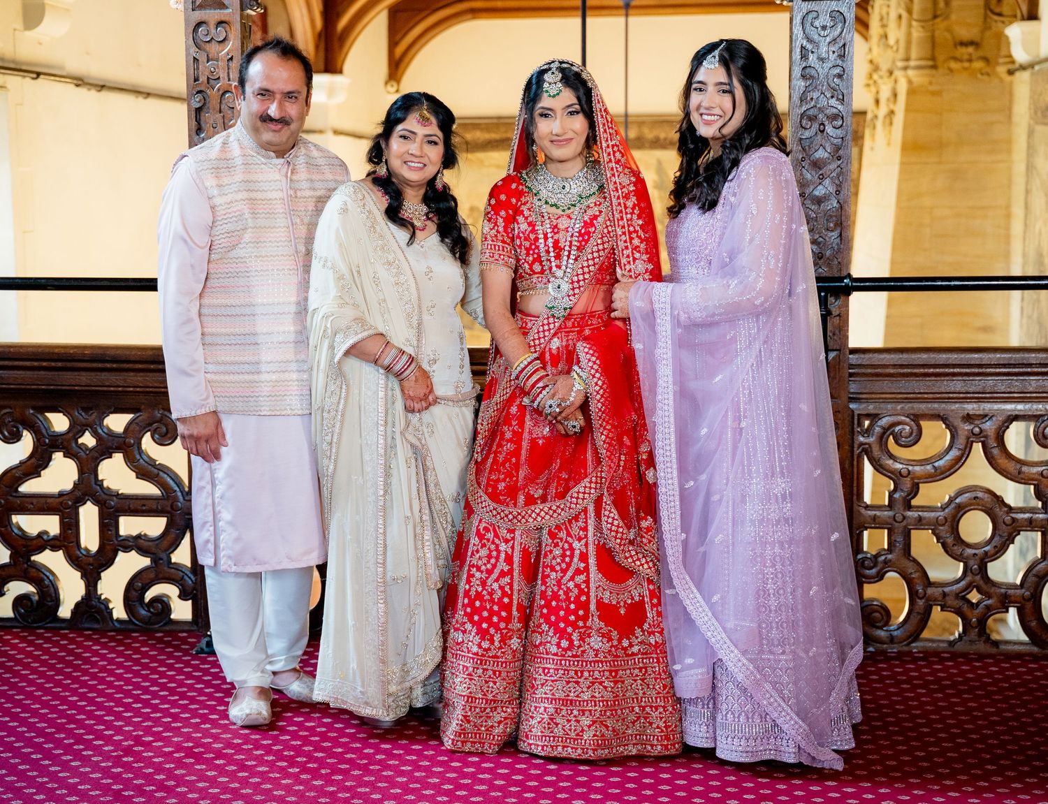 Indian bride in red bridal lehenga posing with family members in traditional attire on balcony.