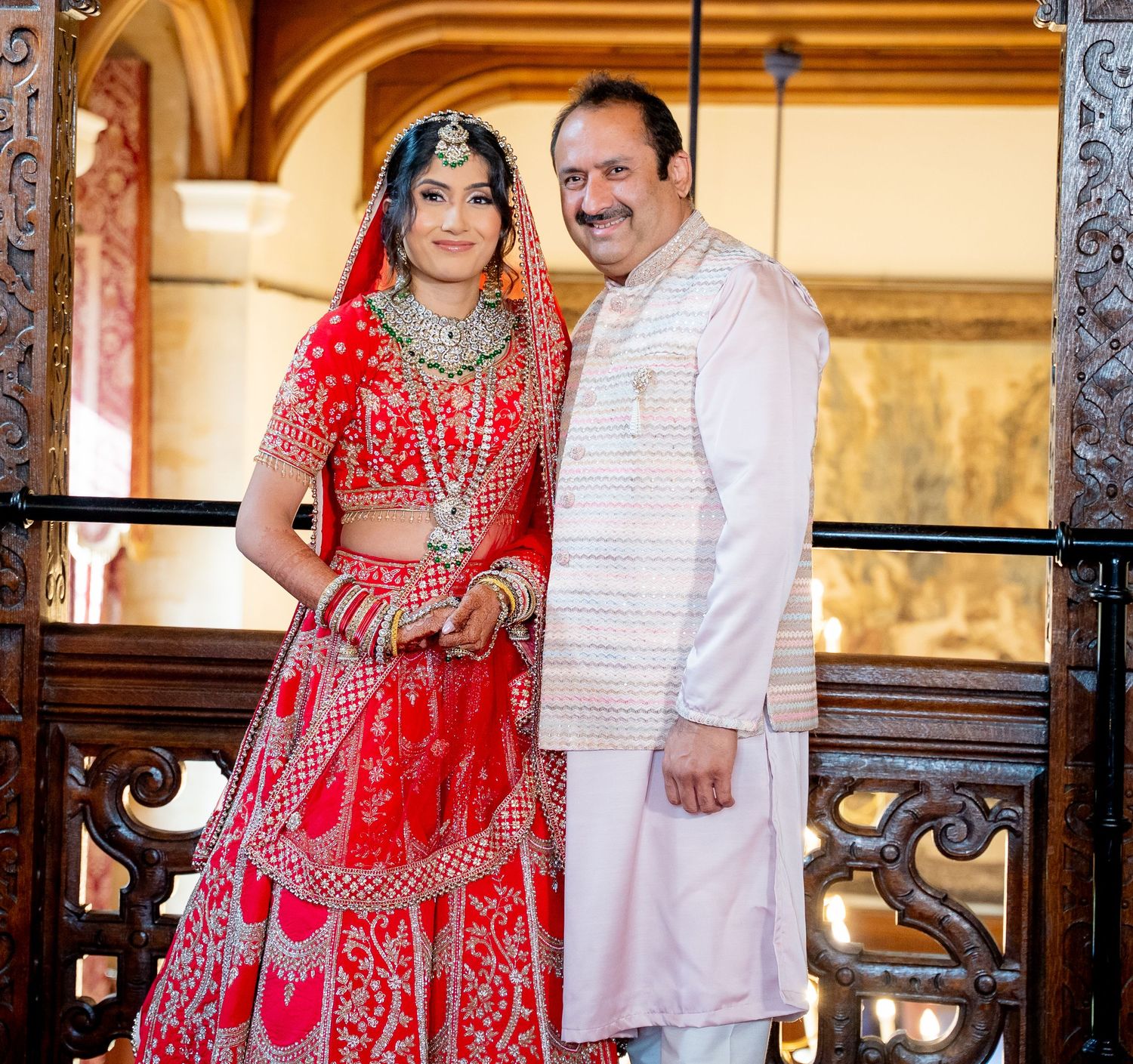 Bride in red bridal lehenga with groom in white kurta posing together at a traditional Indian wedding.
