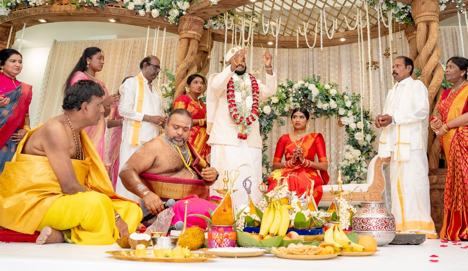 Traditional South Indian wedding ceremony with bride in red saree and groom in white dhoti at decorated mandap.