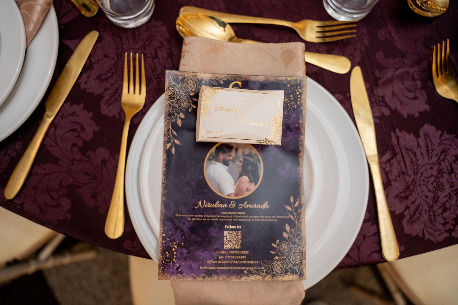 Elegant wedding place setting with gold cutlery, purple damask tablecloth, and personalized menu card with couple photo.