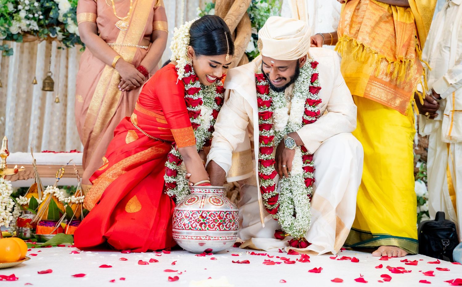 Indian couple performing traditional Hindu wedding ritual with red rose petals and ceremonial pot.