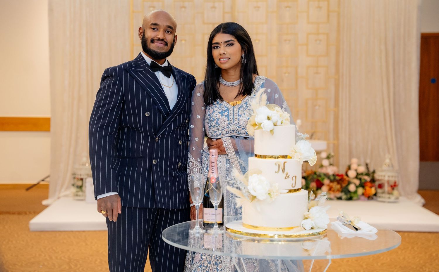Bride and groom smile together beside elegant multi-tiered wedding cake at reception.