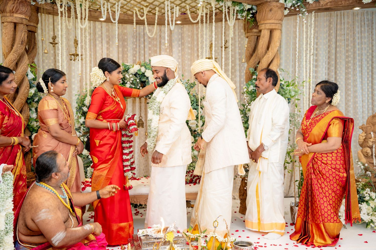 South Indian Hindu wedding ceremony with couple exchanging garlands under decorated mandap surrounded by family members.