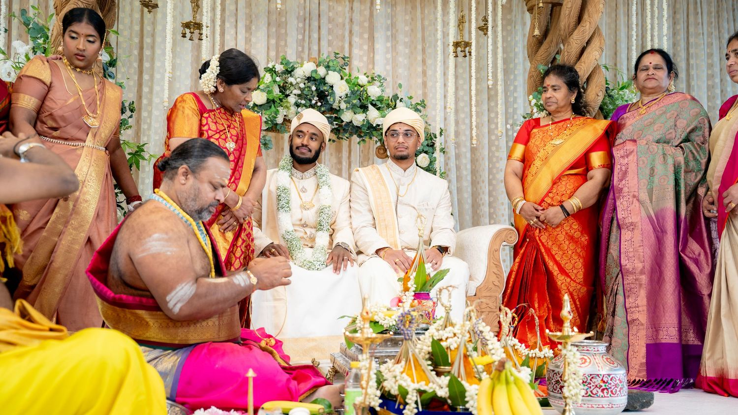 Traditional South Indian wedding ceremony with two grooms seated at decorated mandap with priest.