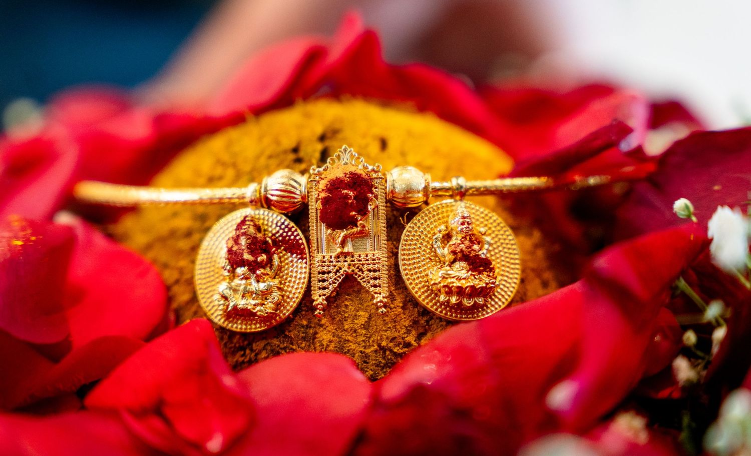 Detailed gold bridal bangle with Lakshmi goddess charms and ruby accents nestled among red rose petals.