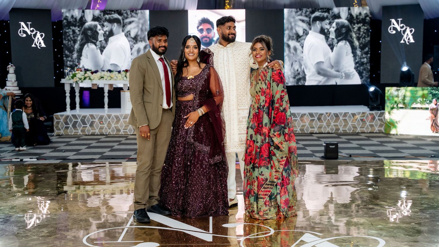 Group of four posing on a reflective dance floor at an Indian wedding celebration.