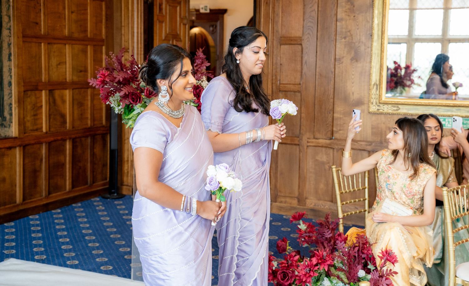 Bridesmaids in lavender sarees carry white flowers during elegant South Asian wedding ceremony.