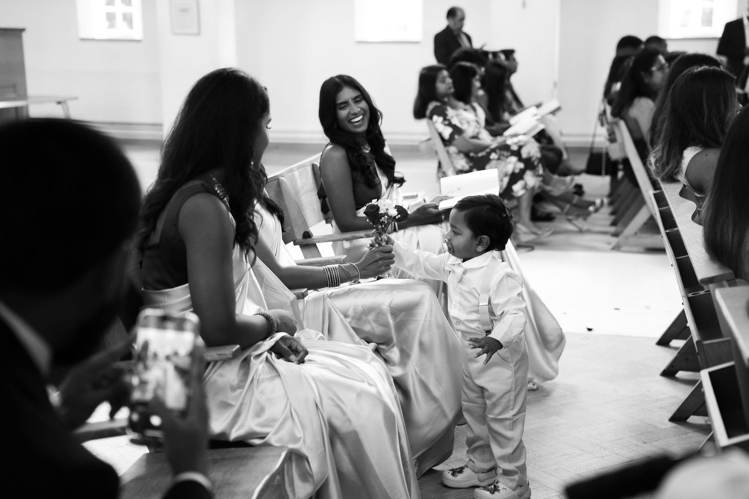 Black and white photo of a smiling bride interacting with a young child at a wedding reception.