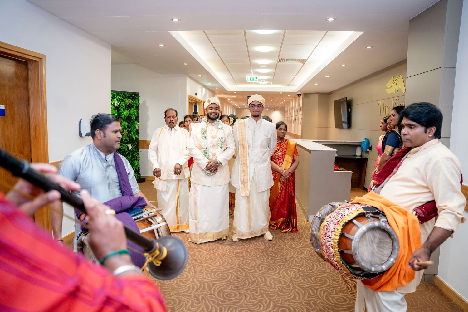 Traditional South Indian wedding ceremony with musicians playing chenda drums welcoming guests in white and gold attire.