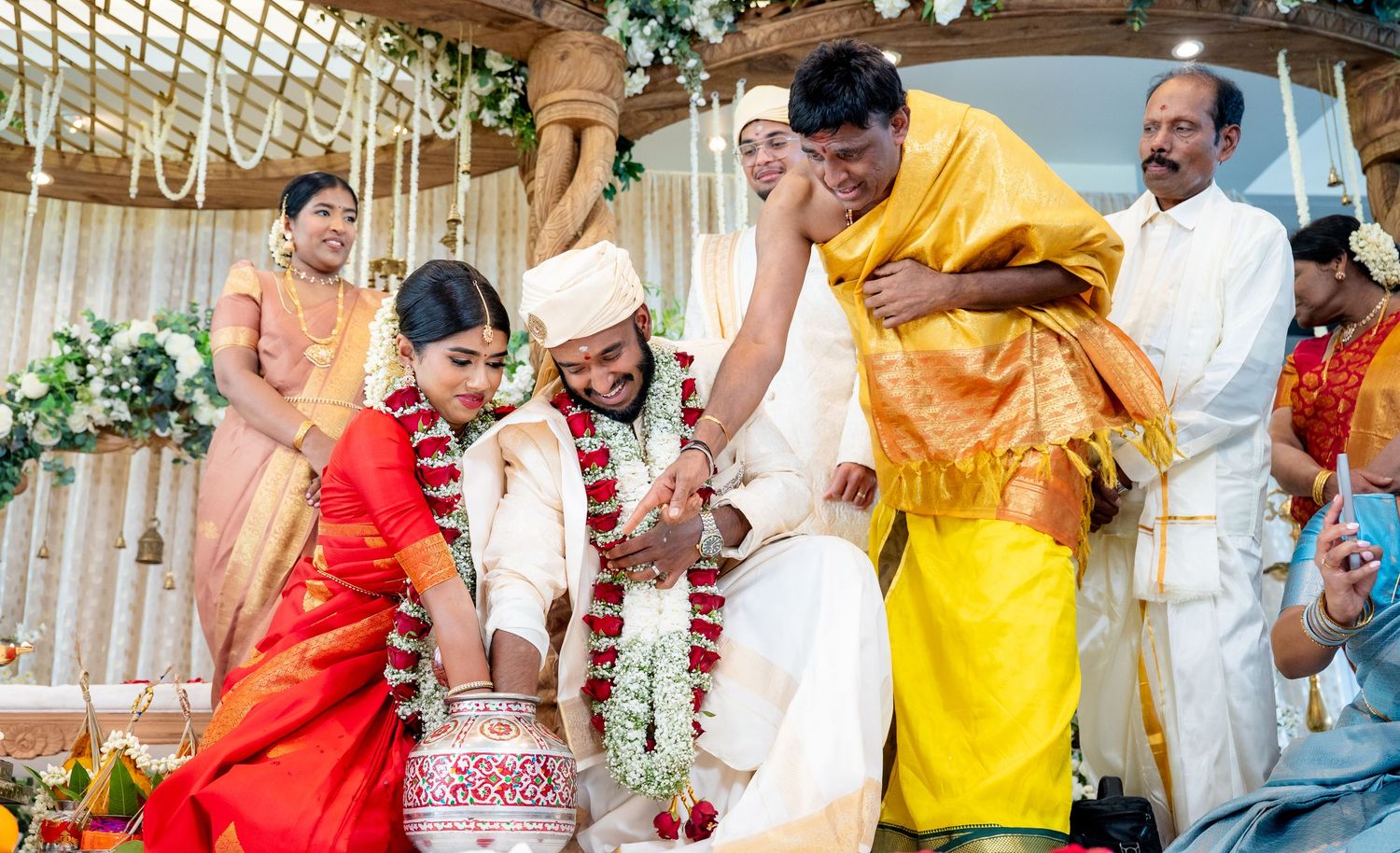 Family members assist the couple during a traditional Hindu wedding ritual on a flower-decorated mandap stage.