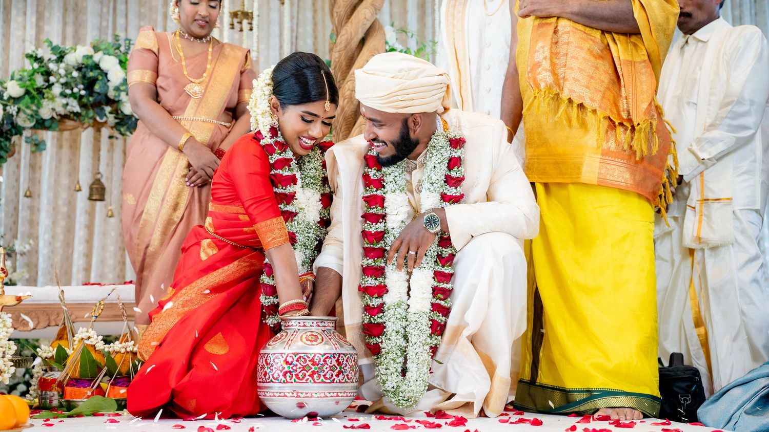 Hindu wedding couple performing sacred rituals with flower garlands at decorated ceremonial altar.