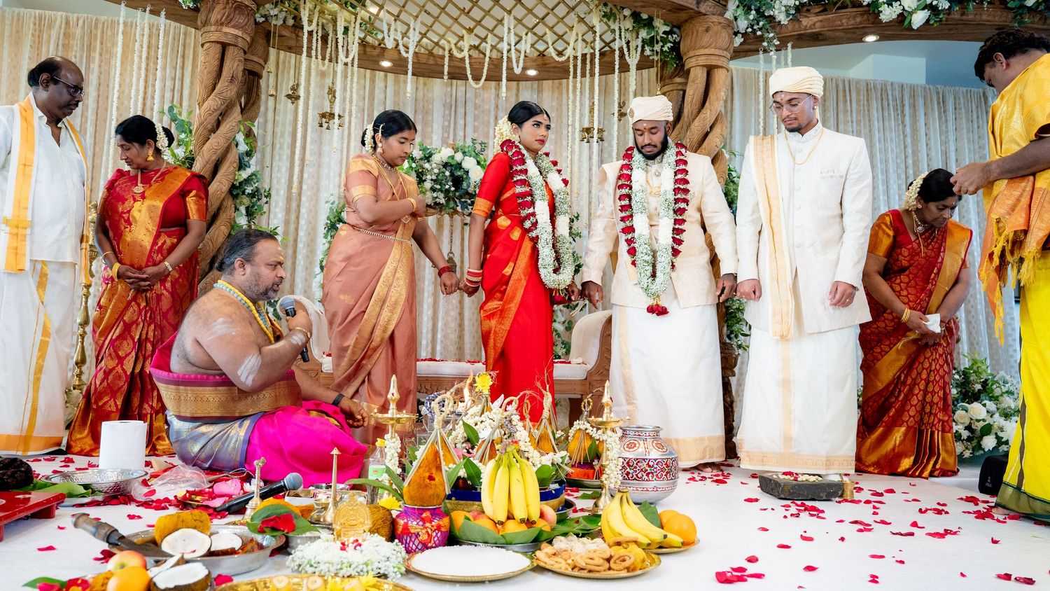 Traditional South Indian Hindu wedding with priest conducting sacred rituals, bride in red saree and groom in white dhoti.