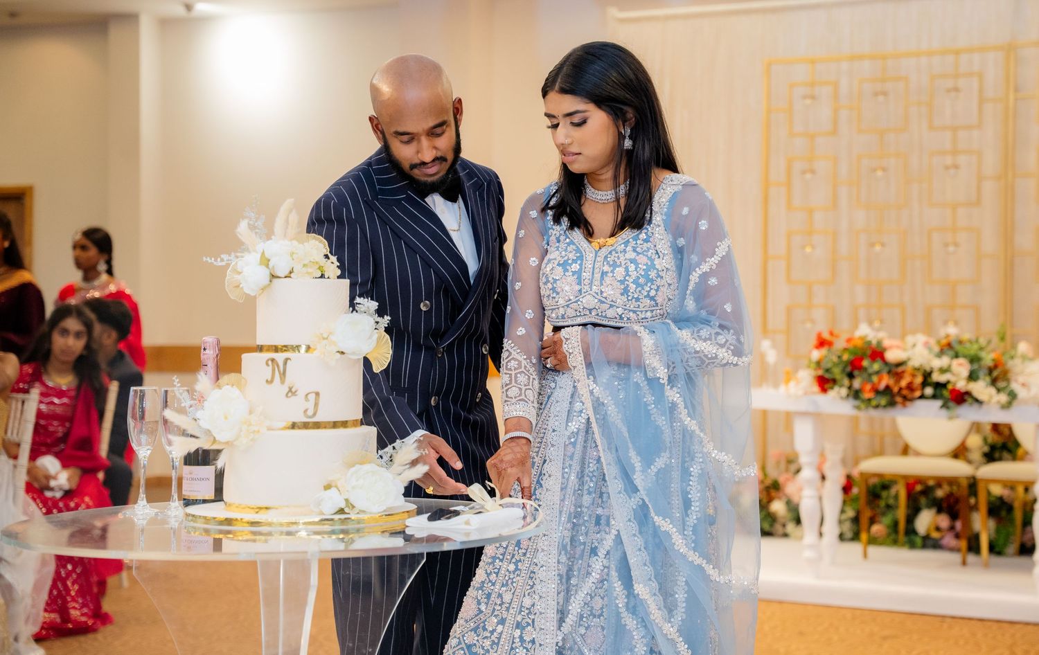 Bride and groom cut their white and gold wedding cake at elegant reception venue.